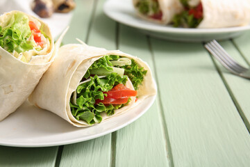 Plate of tasty lavash rolls with tomatoes and greens on green wooden background