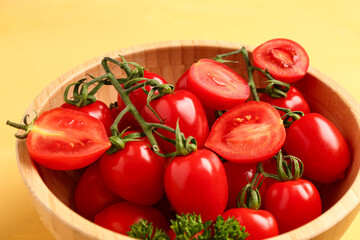 Wooden bowl with fresh cherry tomatoes and parsley on yellow background
