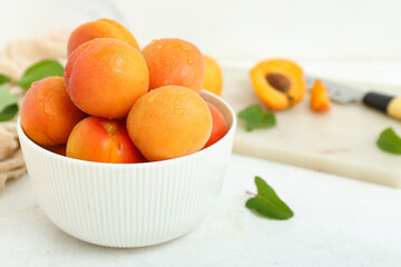 Board and bowl with fresh apricots on white background