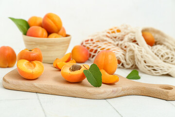 Board and bowl with fresh apricots on white tile table