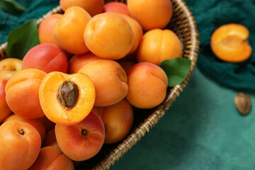 Wicker bowl with fresh apricots and leaves on green background