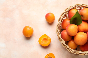 Wicker bowl with fresh apricots on beige background