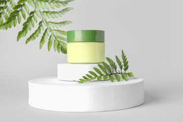 Composition with jar of cosmetic product, plaster podiums and fern leaves on light background