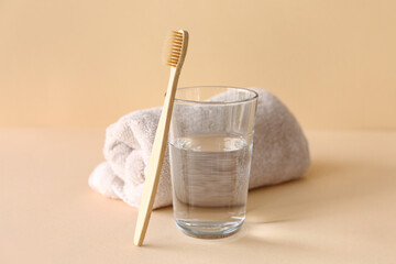 Bamboo tooth brush, glass of water and towel on beige background