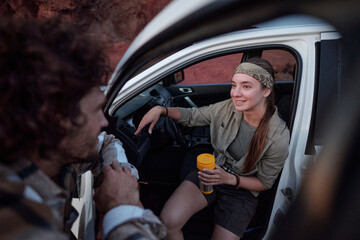 Happy young female backpacker with metallic cup of tea sitting in pickup truck and looking at her...