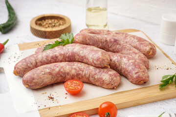 Wooden board with raw homemade sausages on light background