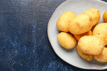 Plate with raw baby potatoes on blue background