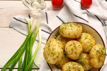 Plate of boiled baby potatoes with dill and tomatoes on white wooden background