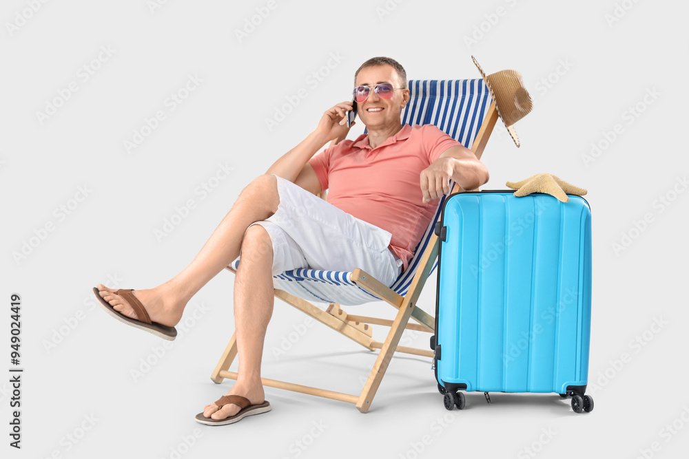 Wall mural Mature man talking by mobile phone in deck chair on light background