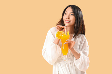 Beautiful Asian woman in beachwear and with cocktail on beige background