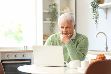 Thoughtful senior man using laptop in kitchen