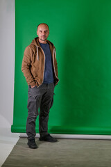 Middle aged bald man in casual attireposes confidently against a green studio backdrop.