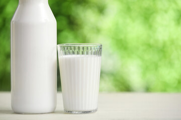 Glass and bottle of fresh milk on yellow wooden table outdoors