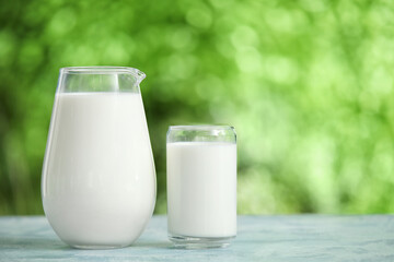 Glass and jug of fresh milk on blue table outdoors