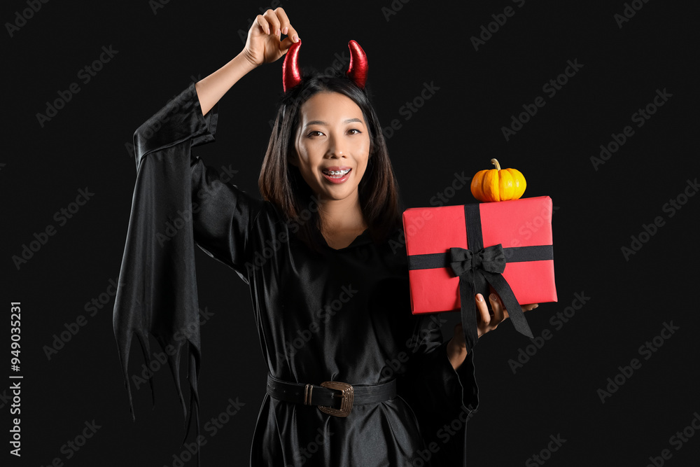 Poster young asian woman dressed for halloween with gift on black background