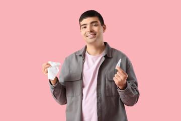 Young man with nasal drops and tissue on pink background