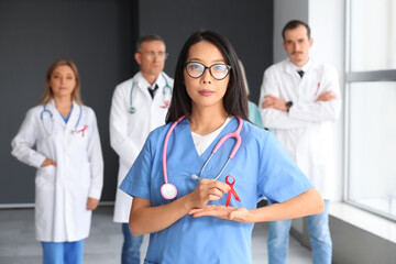 Young female medic with red ribbon and group of doctors in clinic. World AIDS Day concept