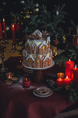 Elegant luxury Christmas table setting for family home party with homemade big gingerbread house, holiday celebration. Red tablecloth, candles, chandelier. Romantic candlelit dinner