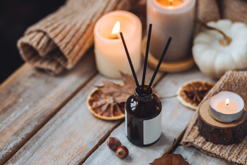 Concept of house decor, apartment seasonal fragrance. Thanksgiving. Autumn mood, cozy fall home atmosphere. Aroma diffuser, pumpkins, knitted warm sweaters, burning candles, dry leaves on wooden table