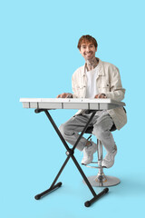 Young tattooed man playing synthesizer on blue background