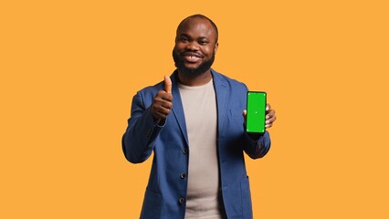 Happy african american man holding green screen phone, doing recommendation. Cheerful BIPOC person presenting mockup device, giving thumbs up sign, studio background, camera B