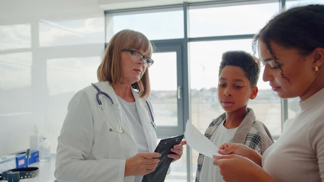 Nurse giving paper from clipboard to woman with son