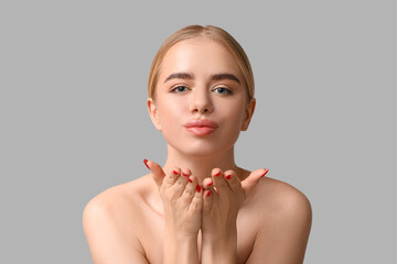Young woman with beautiful lips blowing kiss on grey background