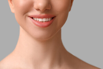 Smiling young woman with beautiful lips on grey background, closeup