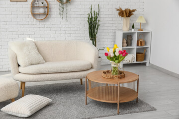 Interior of white stylish living room with sofa, vase with flowers, coffee table and shelving unit