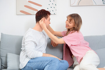 Young couple putting hearing aid on sofa at home