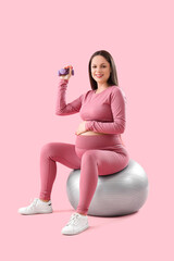 Sporty pregnant woman with dumbbell training on fitball against pink background