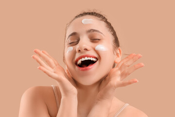 Young woman with facial cream on beige background, closeup