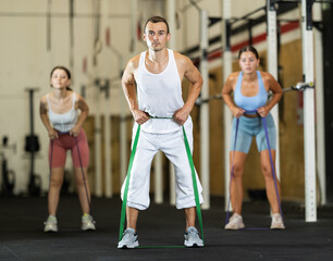 Obraz premium Active man wearing sport clothes using resistance band during group workout in gym. Functional training and CrossFit concept