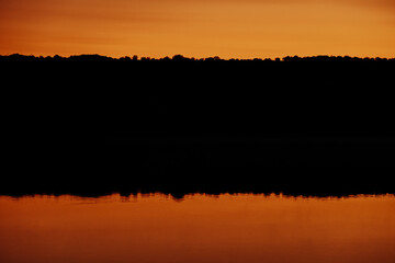 A stunning sunset casts a warm glow, mirrored on still waters, ideal for nature lovers seeking peace and beauty