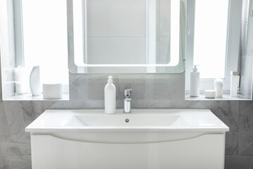 White bathroom washbasin with modern led lighting mirror, stainless steel faucet, bottle of hand soap