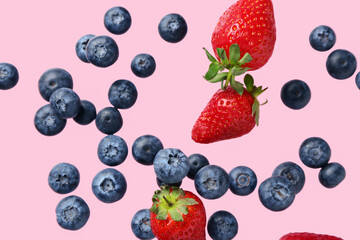 Flying fresh blueberries and sweet strawberries on pink background