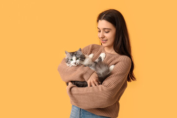 Young woman with cute longhaired cat on orange background