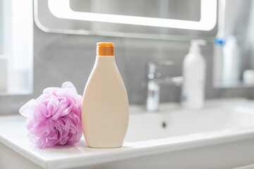 Empty bottle of shower gel and pink sponge on white sink in bathroom, mockup with free space for...
