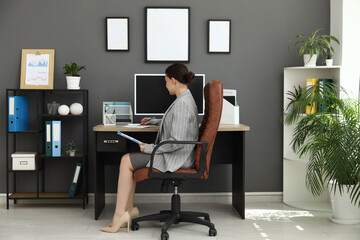 Female office worker with clipboard sitting on armchair and doing paper work at workplace in stylish office