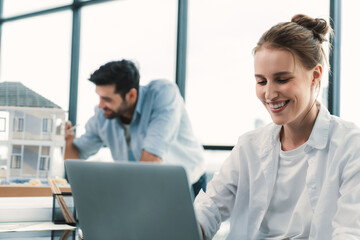 Young skilled project manager working by using laptop while caucasian engineer inspect house mode, using project plan at modern office or architect studio. Civil engineering, creative design. Tracery.
