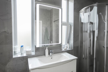 Minimalist bathroom interior with mirror with led lighting above white sink on wall with grey tiles