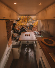 Autumn Vanlife Couple Digital Nomads Camping in New England Fall Foliage. Camper Van Interior Camera, Coffee Cup, Pumpkins, Campfire Burning