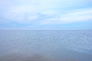 Fototapeta premium Ein weiter Blick auf das Meer unter einem blauen, bewölkten Himmel vermittelt Minimalismus und Einsamkeit