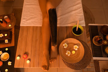 Young woman with mud on her leg in dark spa salon, top view