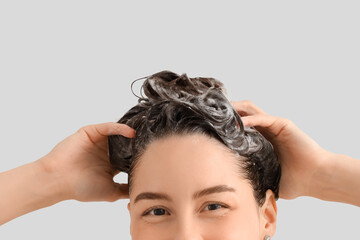 Fototapeta premium Beautiful young happy woman washing her hair with shampoo on white background, closeup