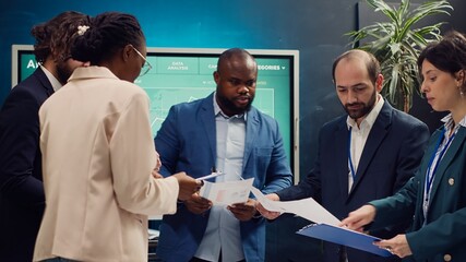 Diverse business affiliates studying market trends by reviewing finances on archived papers, look into budgeting and financial projections. Coworkers attend an information sharing meeting. Camera A.