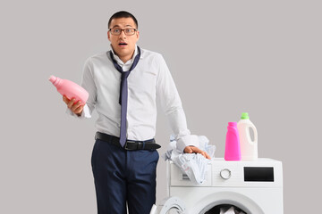 Confused young businessman with bottles of laundry detergent on washing machine against grey...