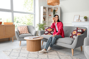 Young woman in eyeglasses sitting on sofa at home