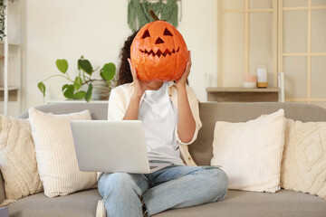 Young woman with Halloween pumpkin shopping online on sofa at home