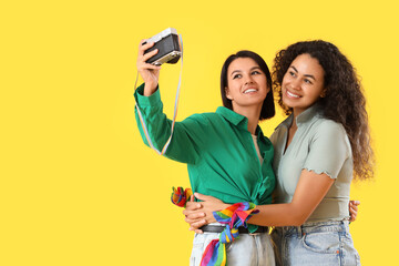 Young lesbian couple taking selfie on yellow background